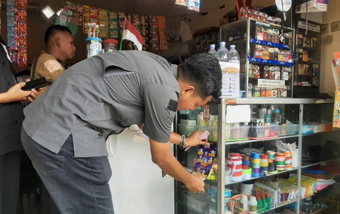 Petugas Bea Cukai saat tempelkan sticker sosialisasi terkait larangan jual beli rokok olegal pada salah satu toko.